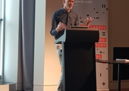A man stands at a lectern with gesturing hands