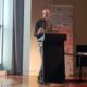 A man stands at a lectern with gesturing hands